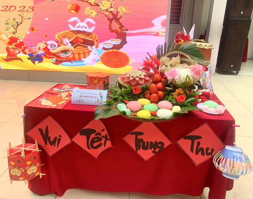 A table with a red cloth with a tray of food and a sign

Description automatically generated